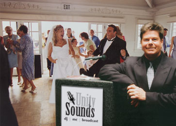 DJ Drew Miller poses with equipment while the newlyweds dance in the background